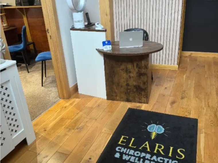 Reception desk at Elaris Chiropractic, with an oak floor and the Elaris branded mat at the entrance